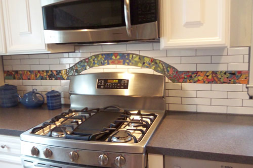 Residential Kitchen Backsplash in Lyric Decades 2 x 8 Subway Tile with custom pique assiette mosaic inset.